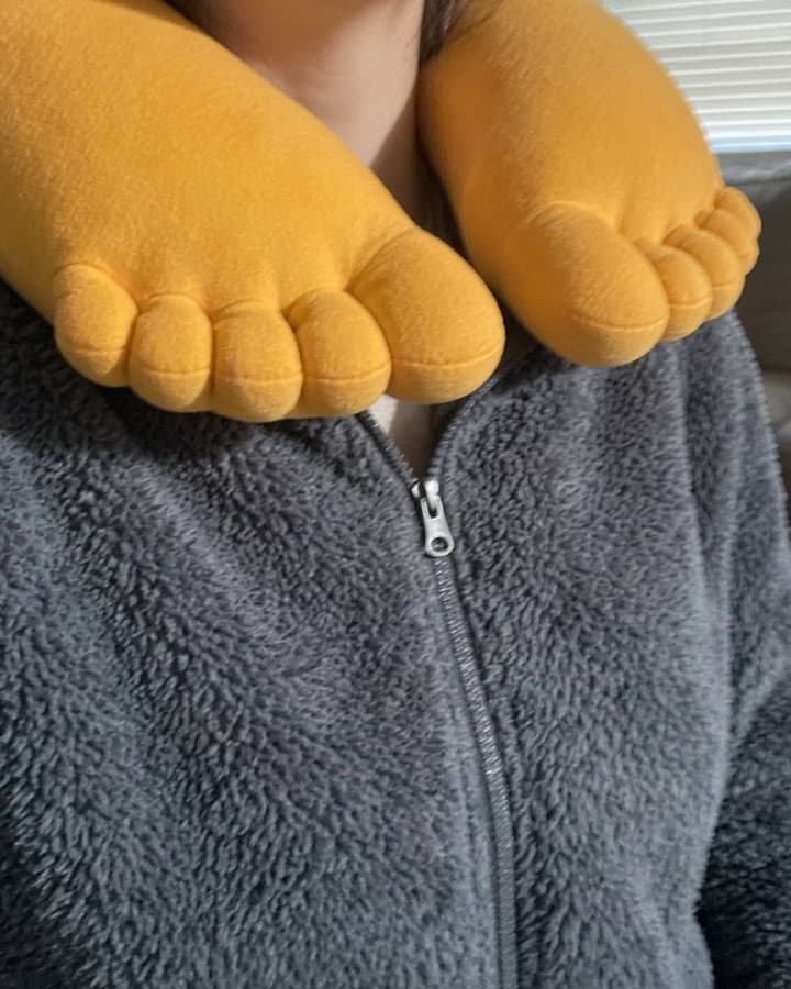Close-up of the toes of a GyatFoot pillow worn around the neck over a grey zip-up jacket